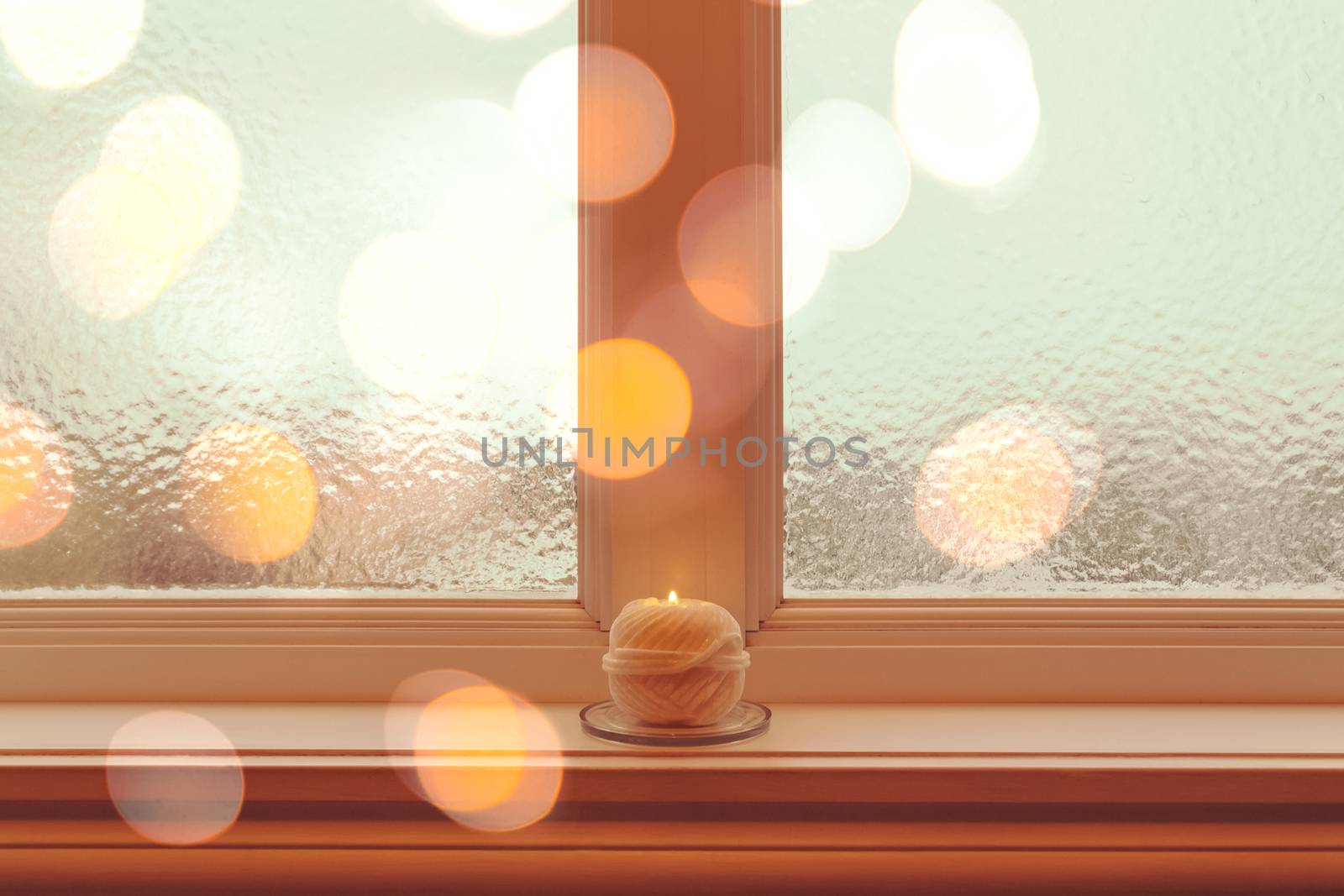 Frosted winter window and a cozy burning candle in golden light.