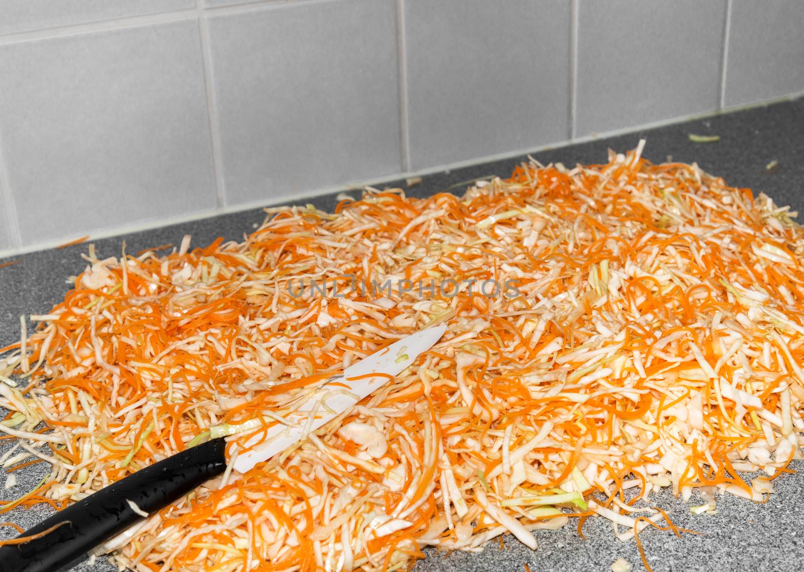 Homemade sauerkraut preparation - fermented cabbage and carrots, rustic winter food. Shredded cabbage, carrots, and knife on kitchen countertop.