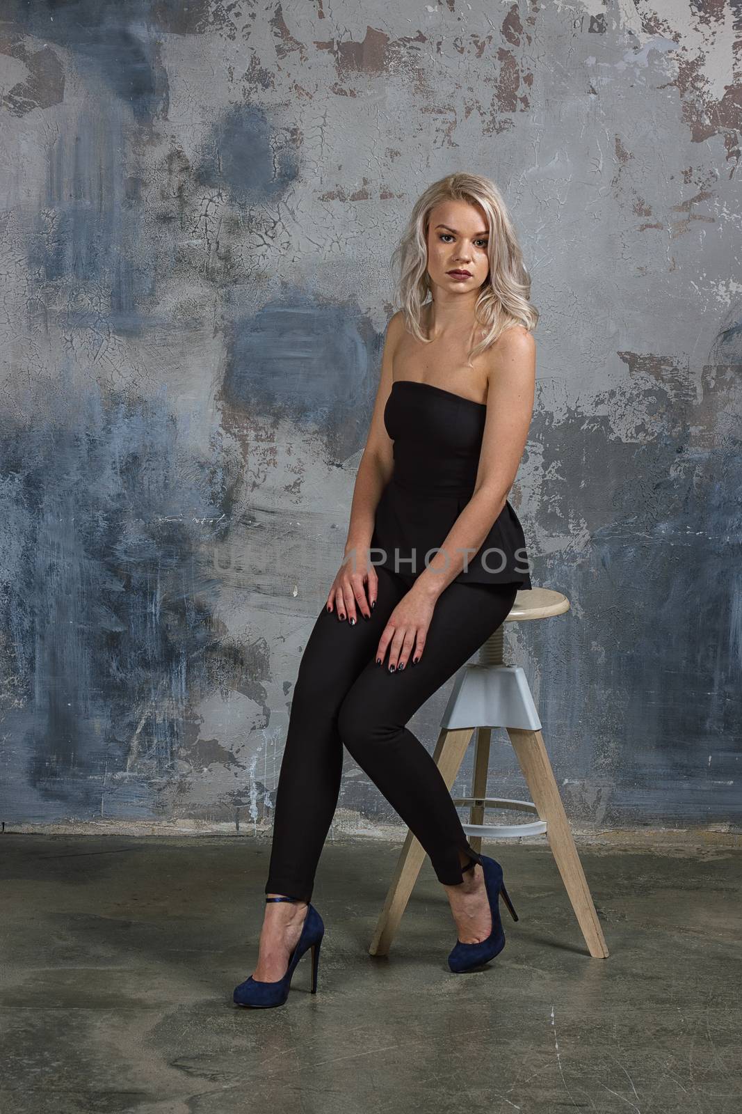 girl in a black dress with long flowing hair sitting on a high chair next to a wall