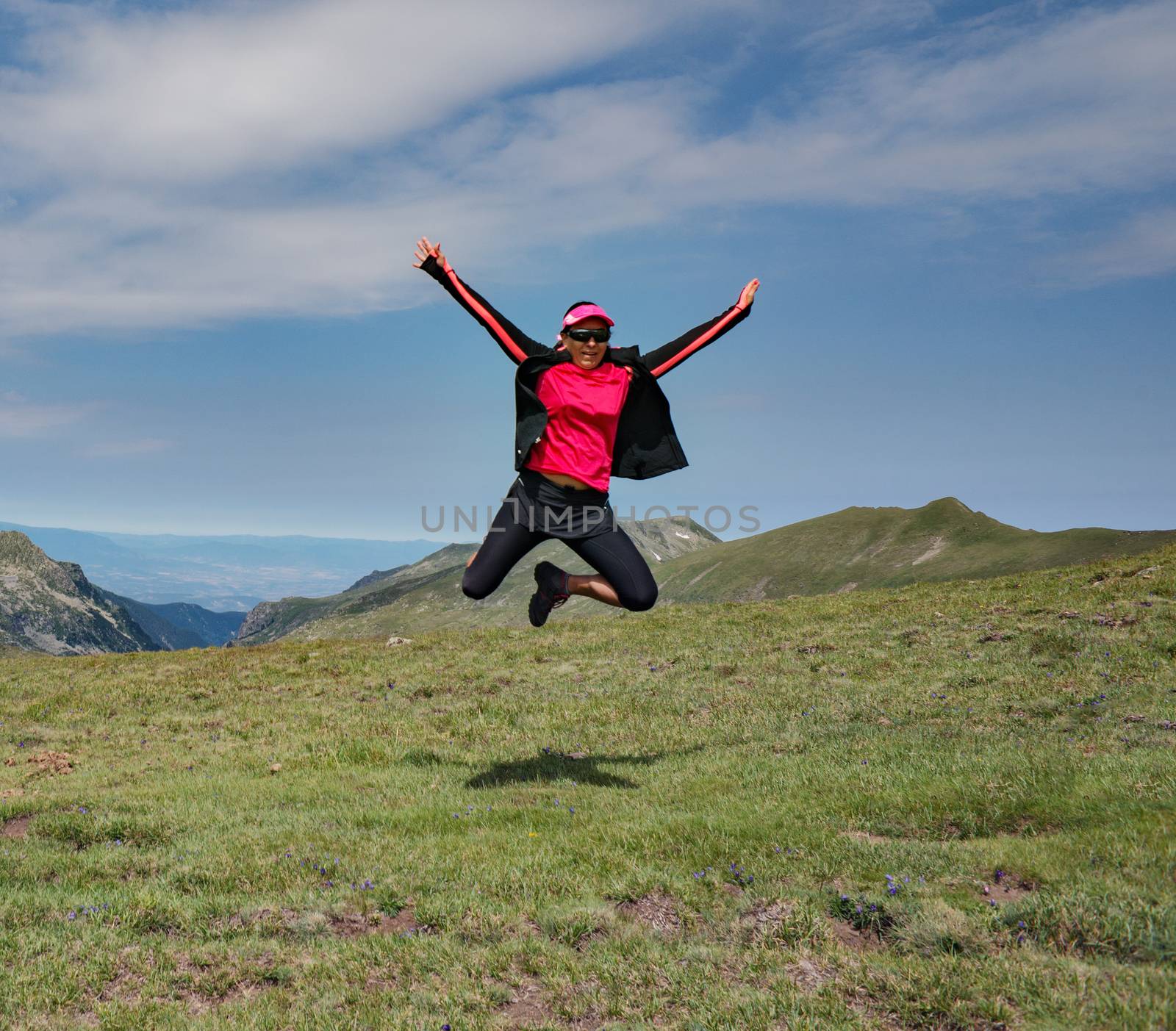 A girl is jumping high in the air with mountains as background.