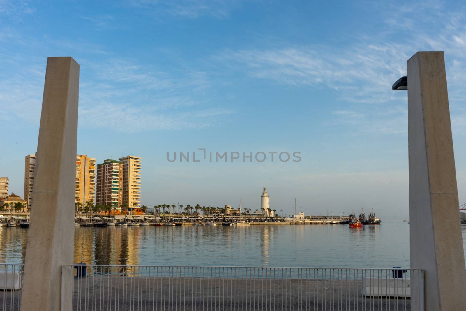 White lighthouse and the tall buildings of Malaga with their reflections in Malaga, Spain, Europe at golden sunset hour