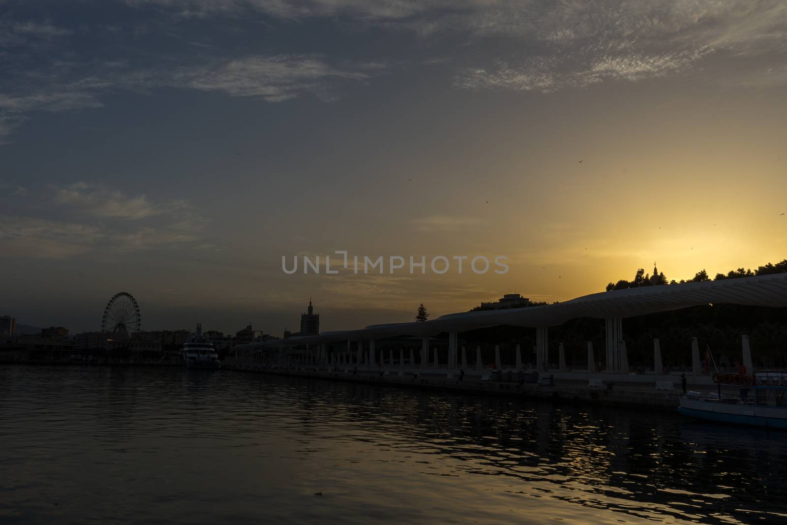 Giantwheel and the docking harbour of Malaga with sun set in the background in Malaga, Spain, Europe at the golden hour