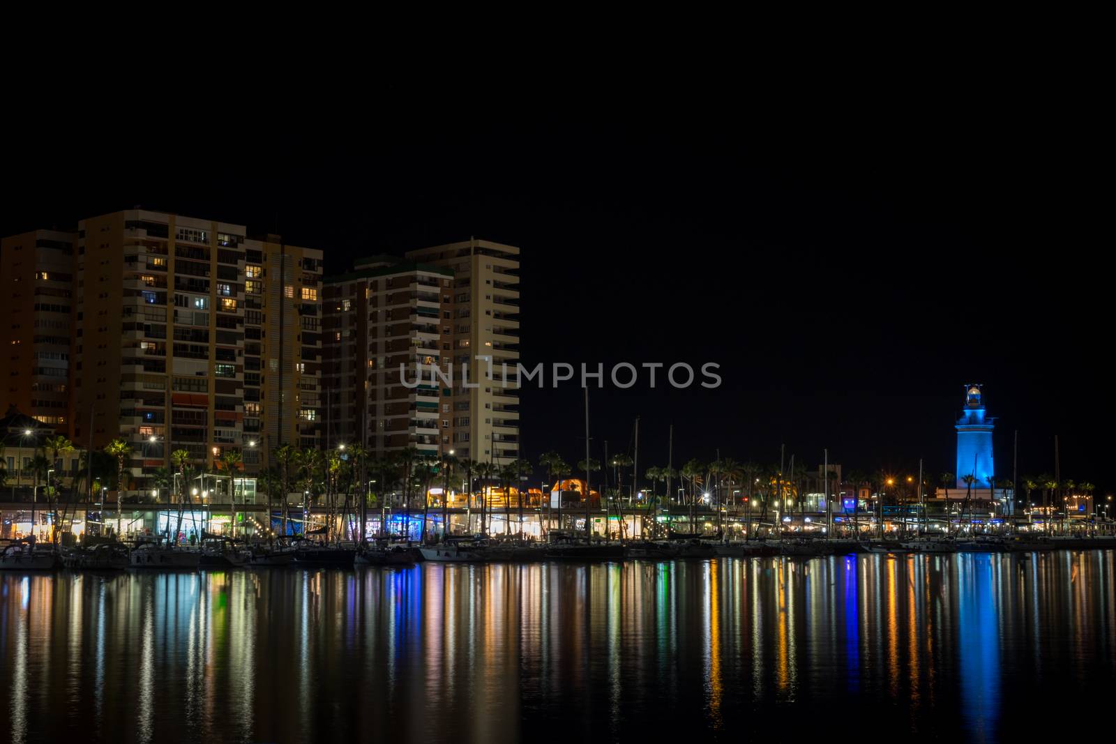 View of Malaga city and lighthouse and their reflections on water from harbour, Malaga, spain, Europe at night with illuminations