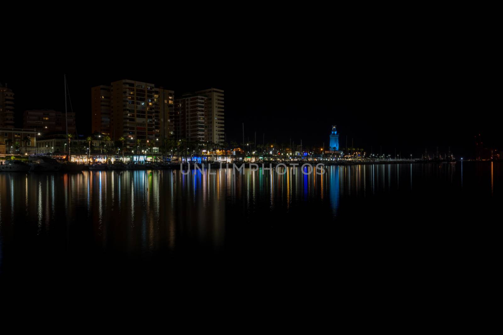 View of Malaga city and lighthouse and their reflections on water from harbour, Malaga, spain, Europe at night with illuminations