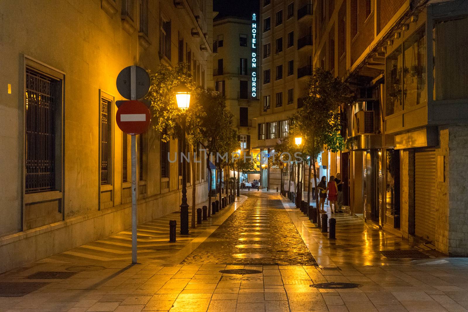 Cobblestone street lit with yellow street lamps at night in Malaga, Spain, Europe