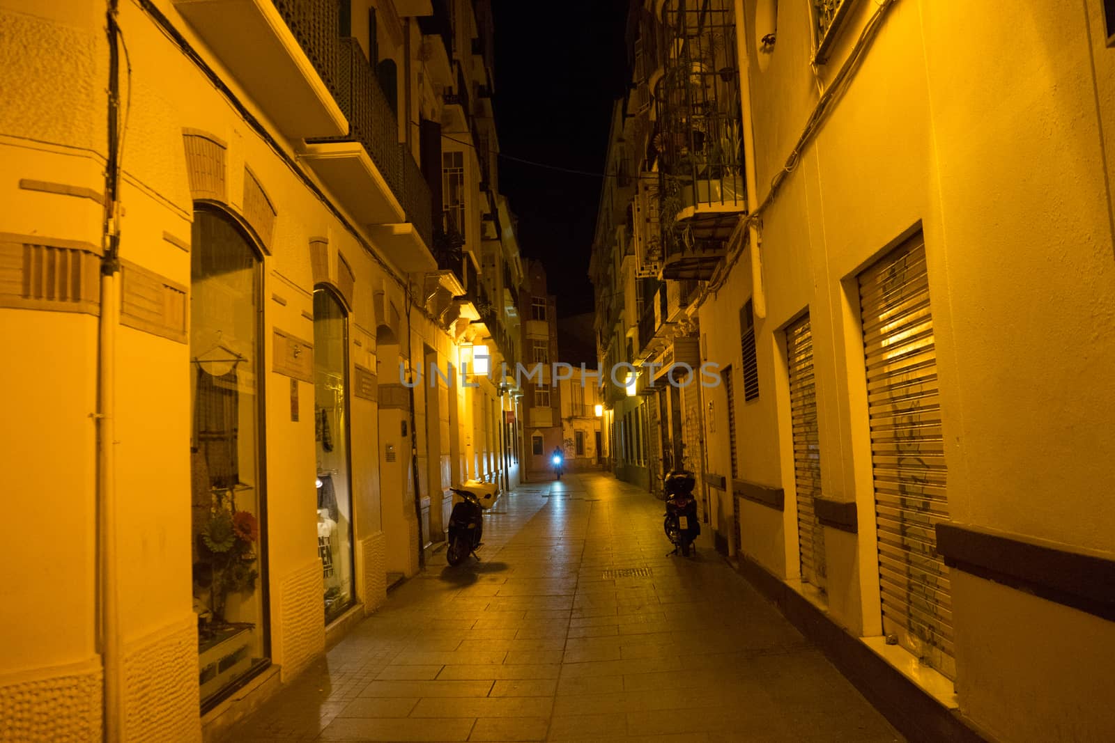 Cobblestone street lit with yellow street lamps at night in Malaga, Spain, Europe