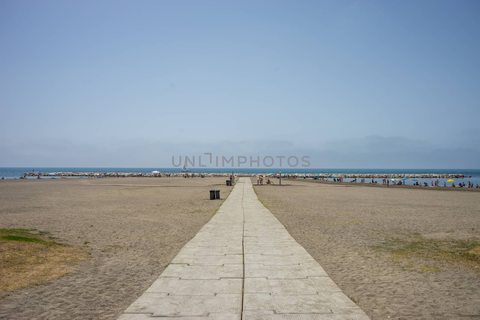 A stone pathway leading to the sea and ocean at Malagueta beach in Malaga, Spain, Europe on a cloudy moring with a boat in the ocean background