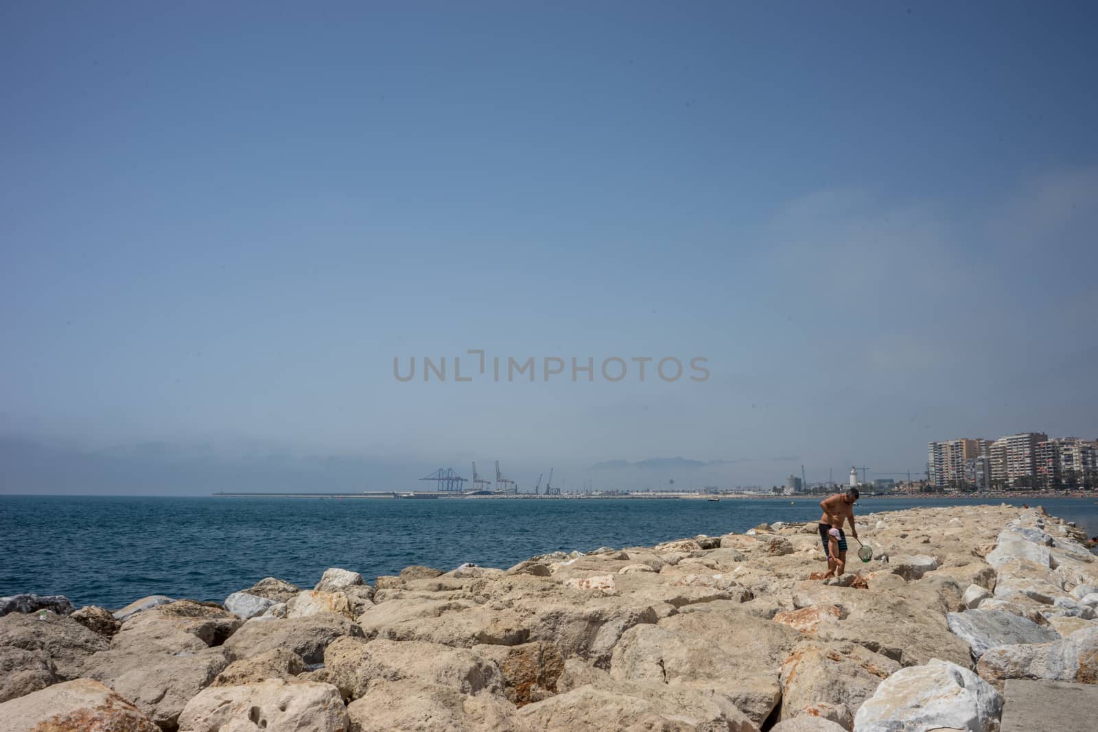 A father helping his son walk on the rocks on the Malagueta beac by ramana16