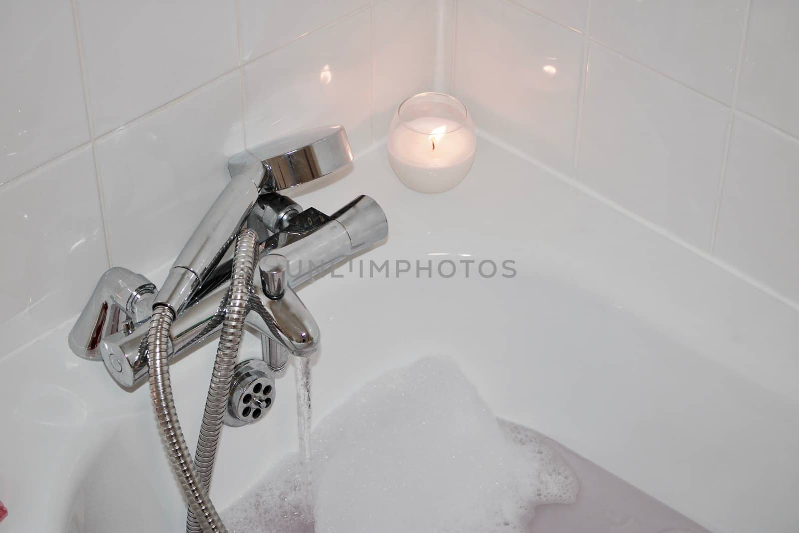 White candle in bathroom near hot water and foam. Bath concept.