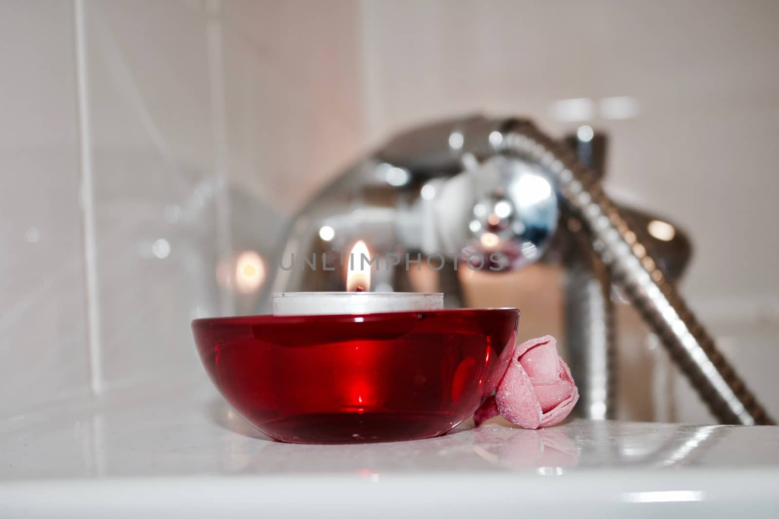 Small candle in red glass holder near silver faucet in bathroom.