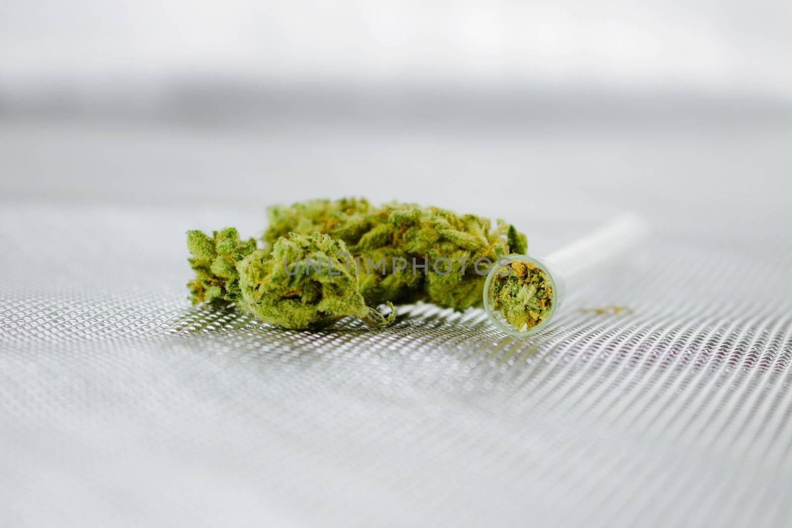Green fresh marijuana leafs on the silver background near glass pipe.