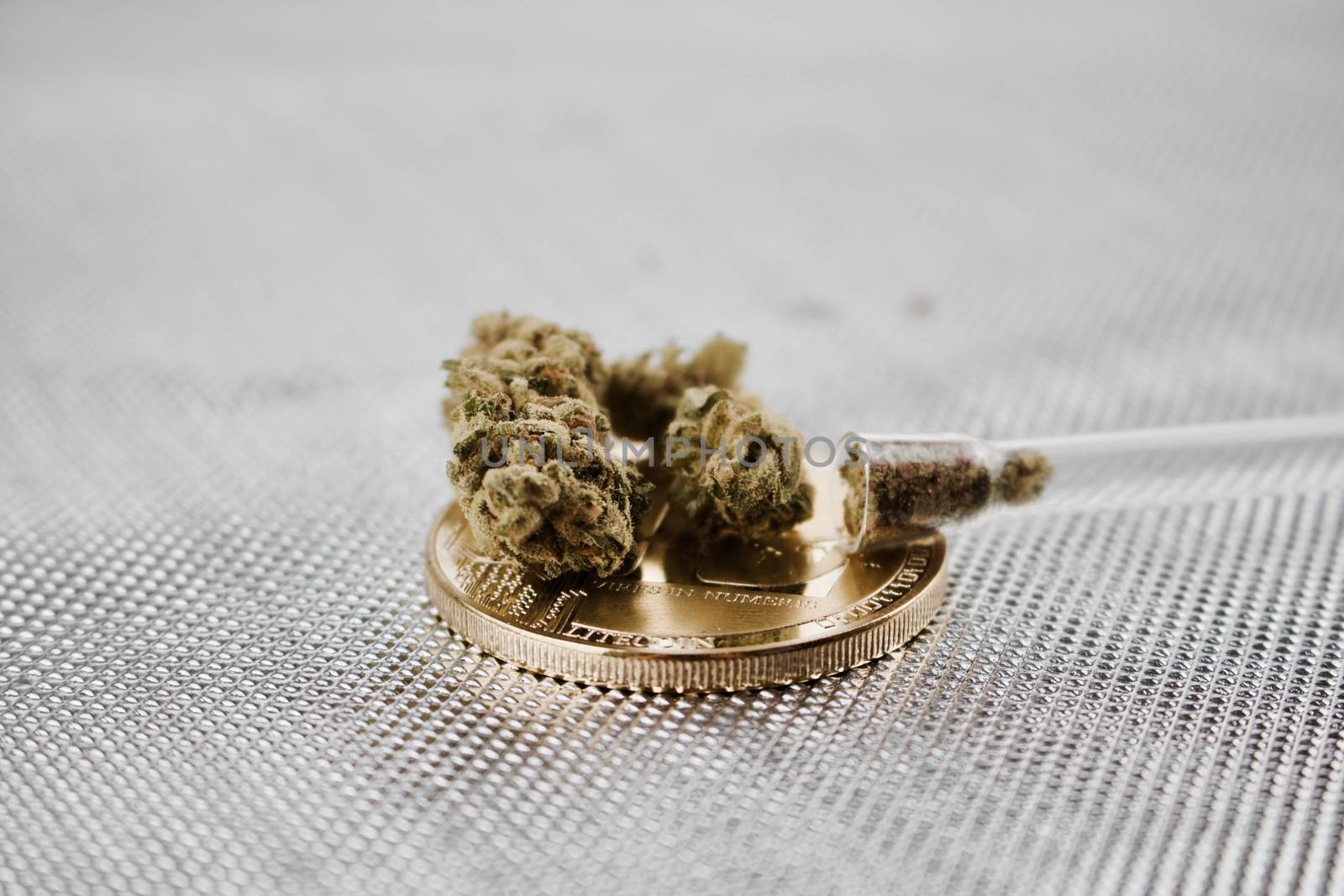 Green fresh marijuana on gold litecoin coin in silver background.
