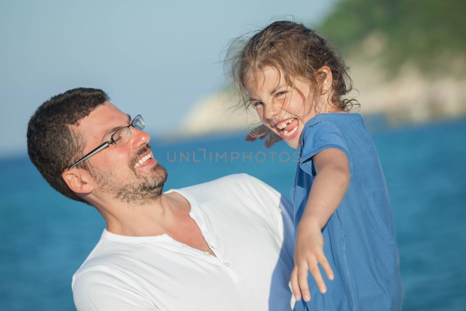 Happy laughing girl being carried by her young father by the sea.