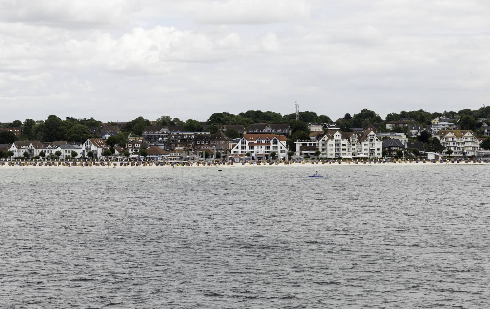 people on the beach with the houses of the german city Kiel as background