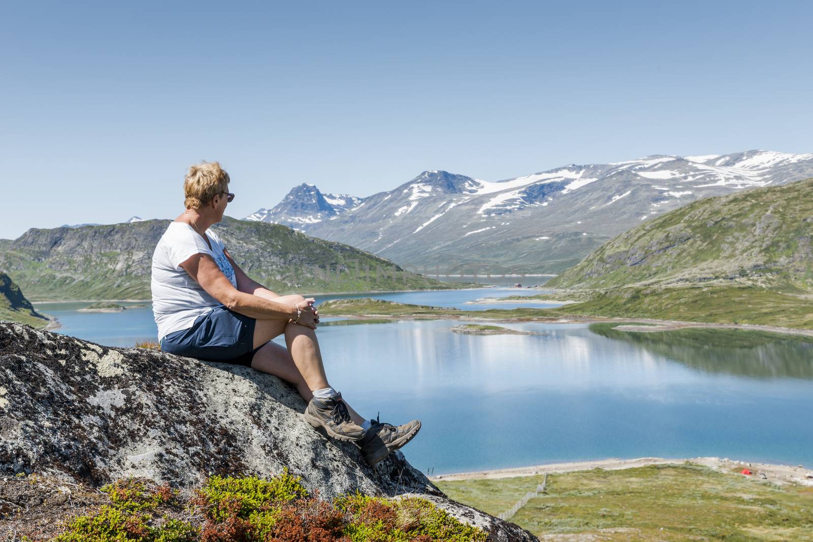 adult woman sittin gon a rock looking over the national park from bitihorn to stavtjedtet with lakes fjord and snow on the mountains