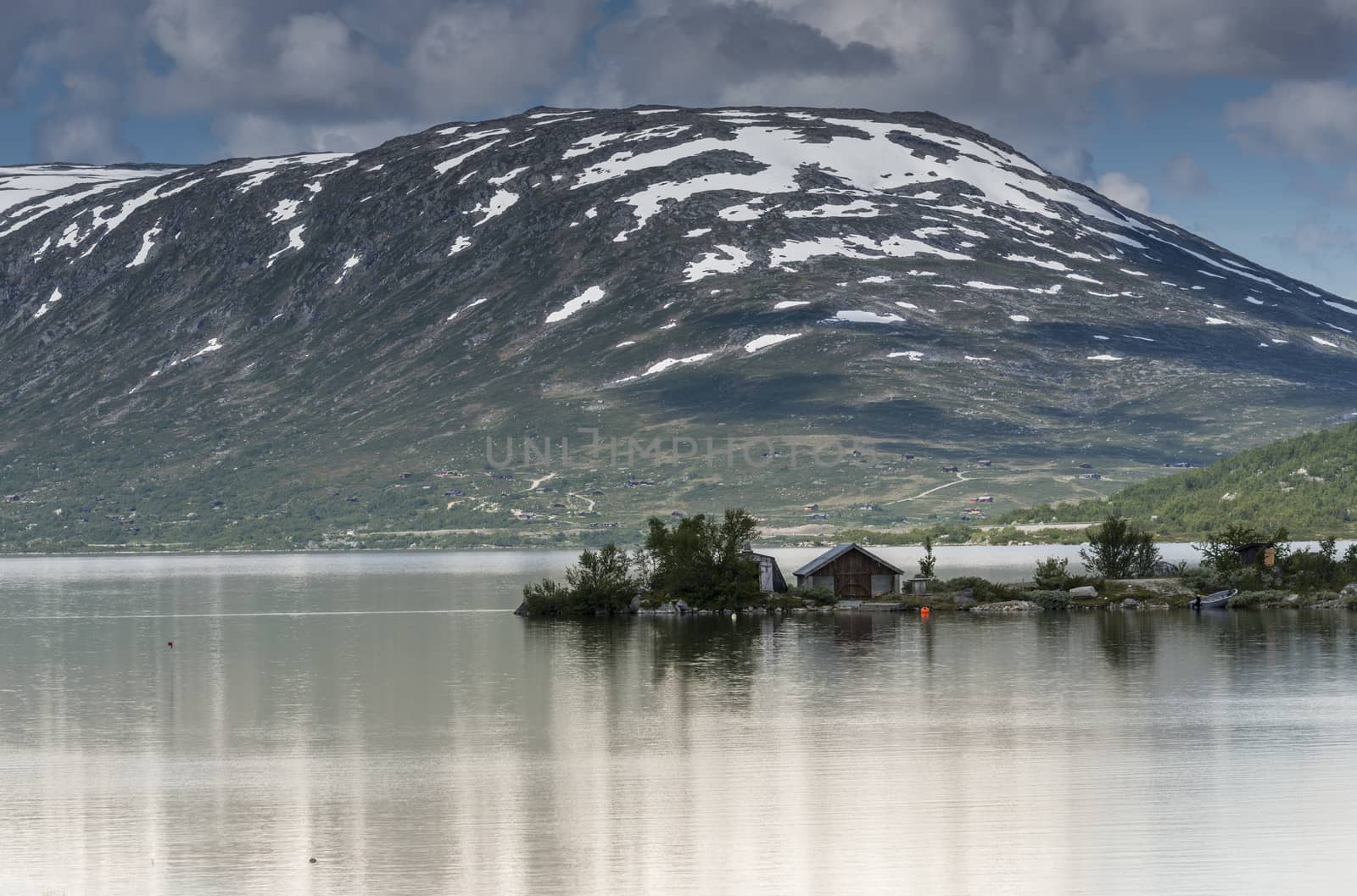 old house at a fjord with mountains with snow in the summer as background