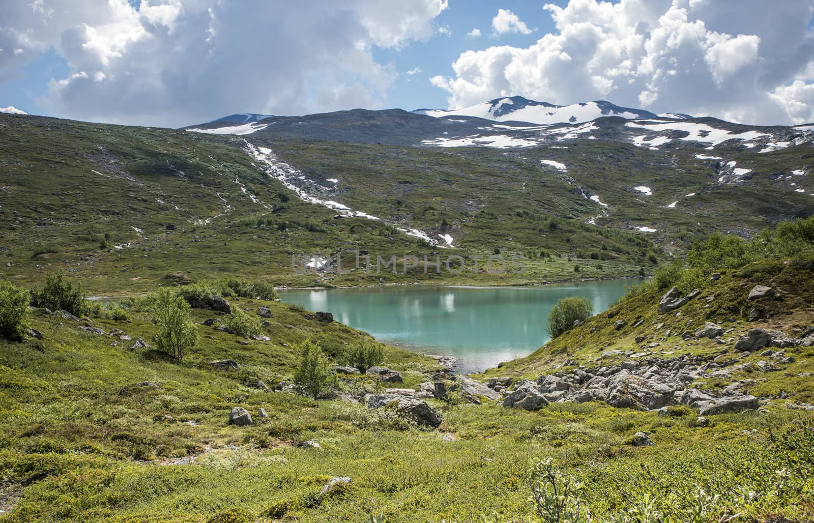 small lake in nature norway near gamle strynefjellsveg with blue water and mountains with snow in background