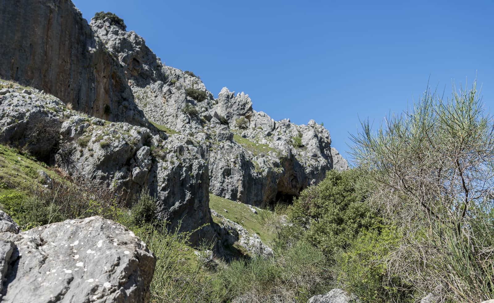 rocks with old ancient caves where people used to live and blue sky in andalusia with green grass landscape