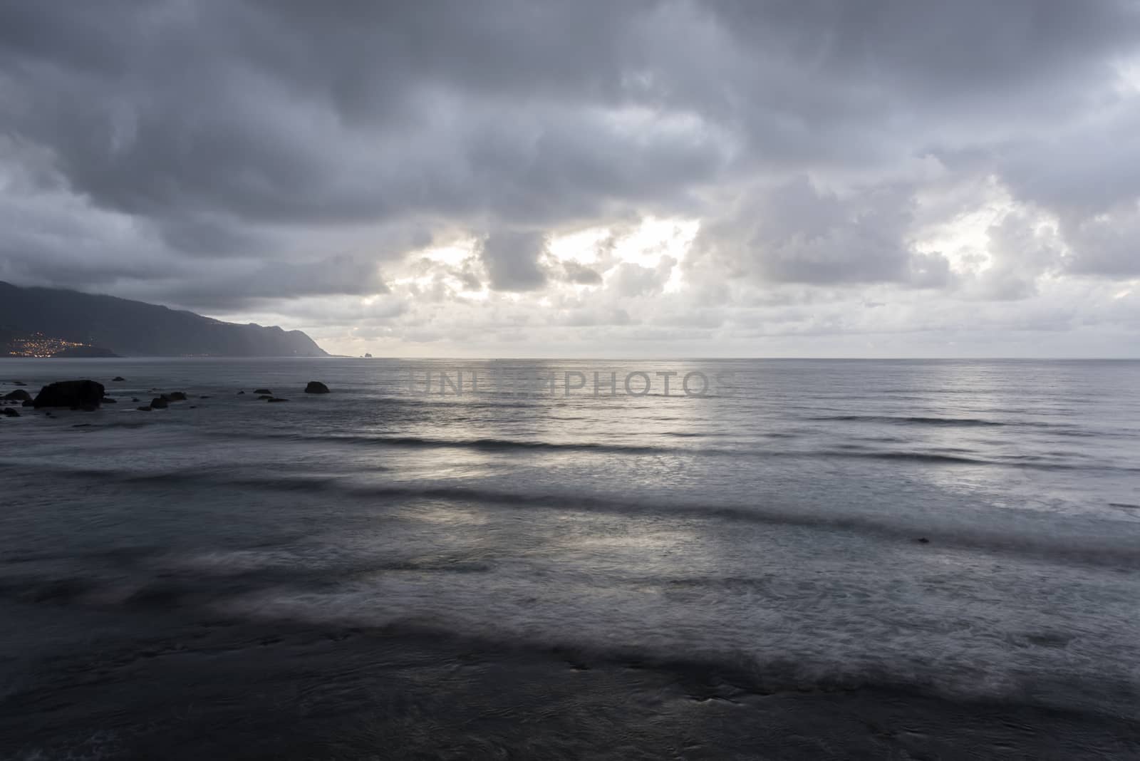 dark clouds in the evening over Madeira island with clouds and rocks and lightened village in background