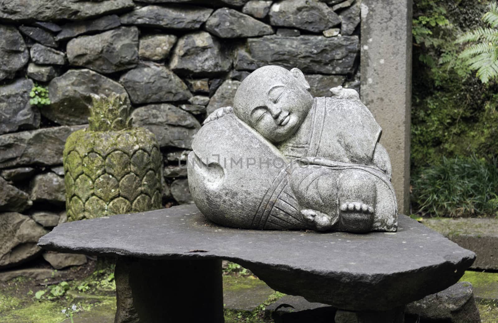 sleeping young buddha statue in garden with green plants and wall with rocks