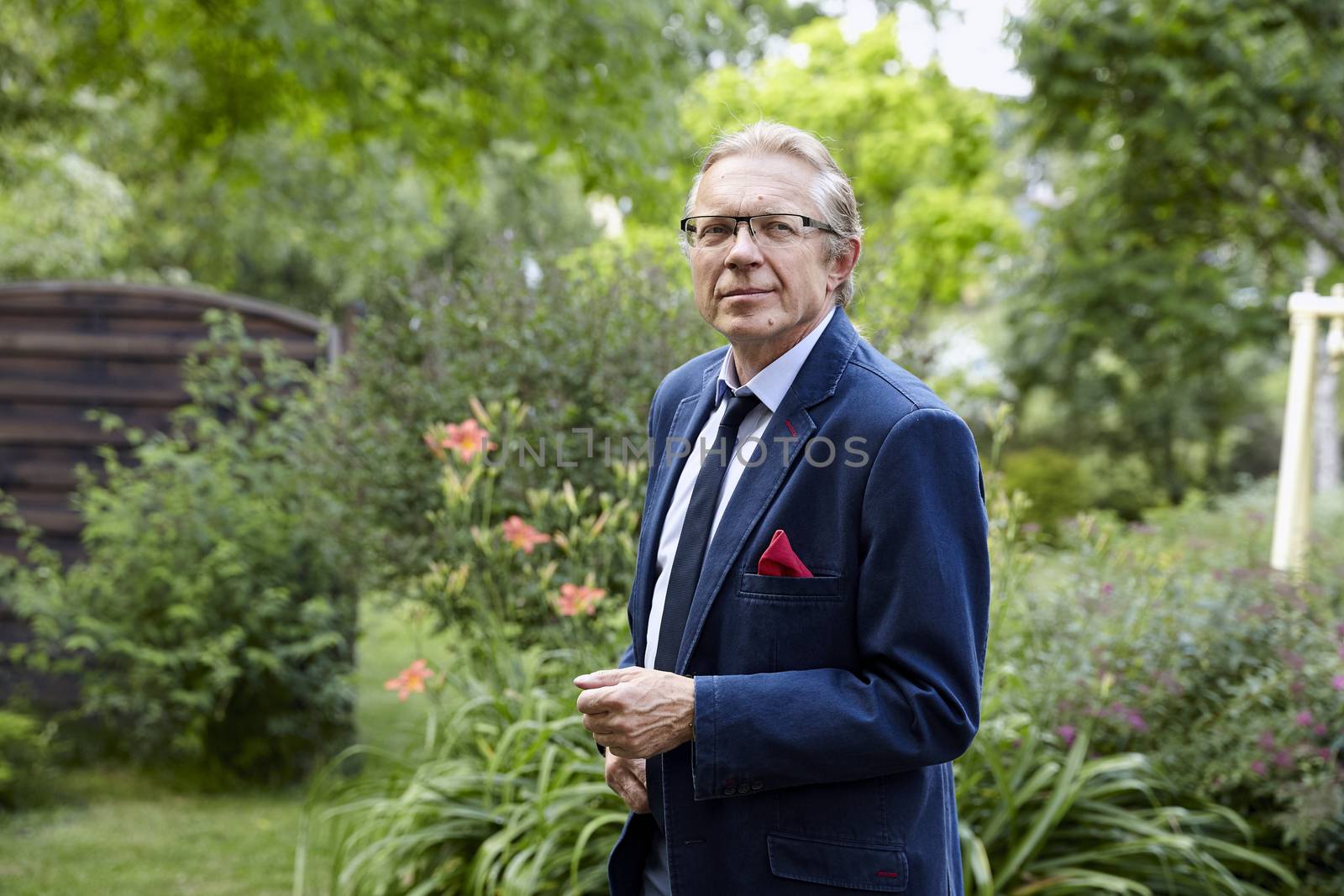 Portrait of middle-aged smiling man wearing blue jacket in the garden. Natural sunlight.