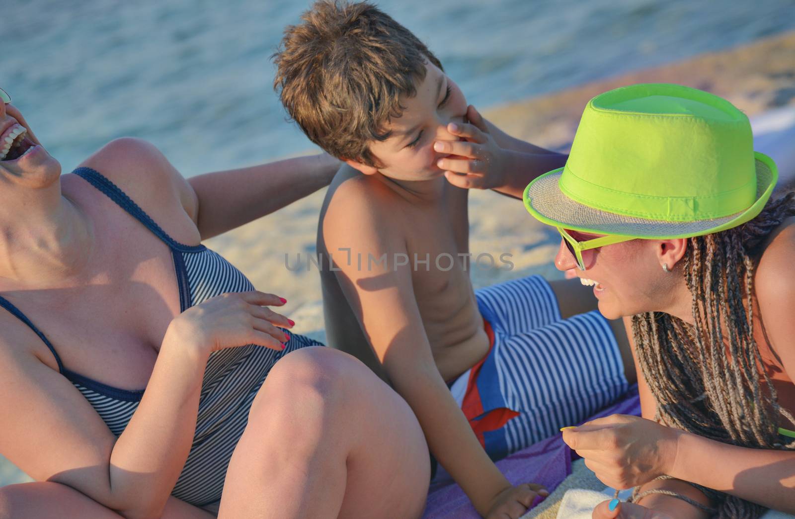 A company of three - two females and a male kid laughing on the beach.