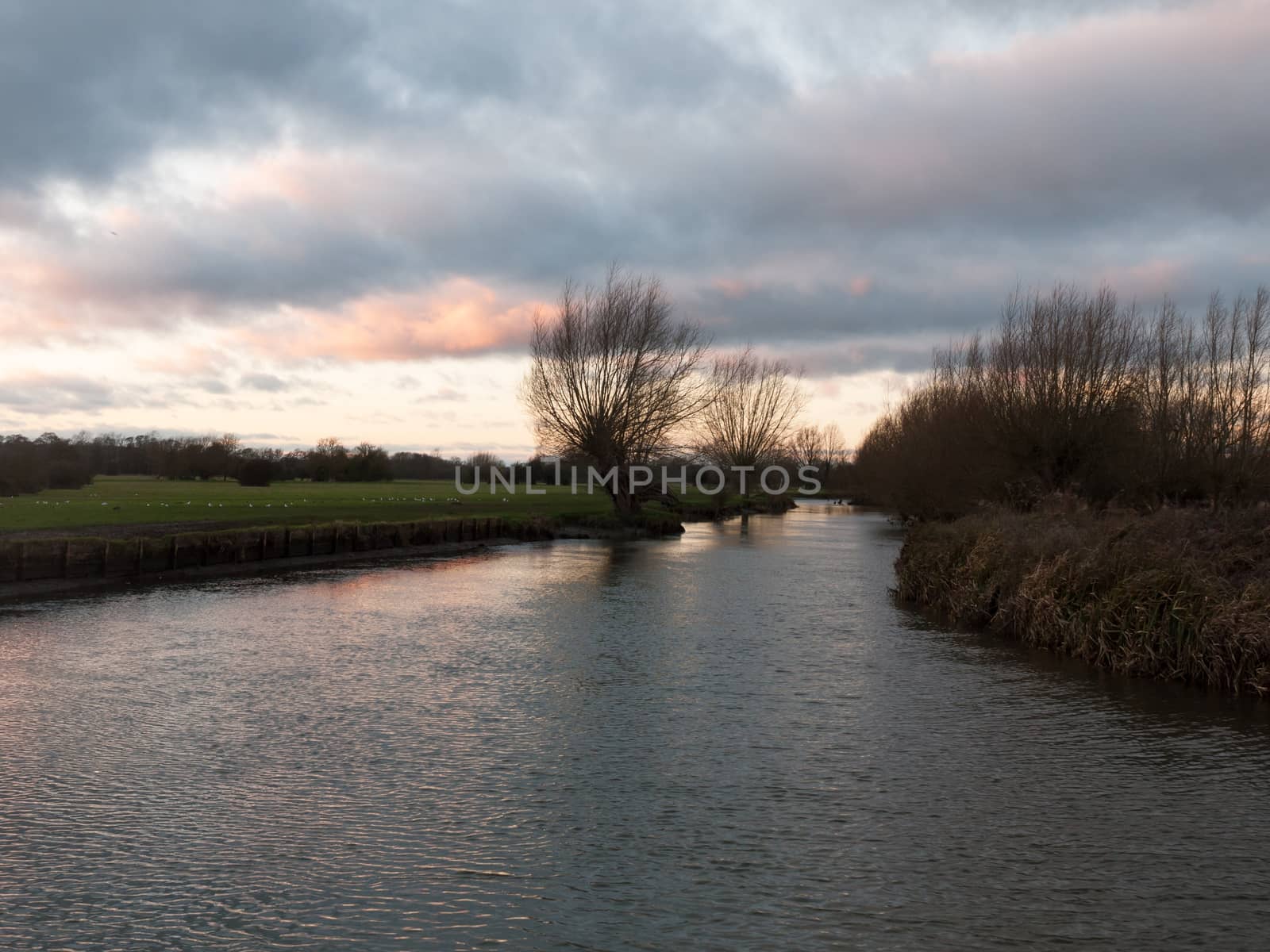 sunset moody sky winter autumn over green field with trees water by callumrc