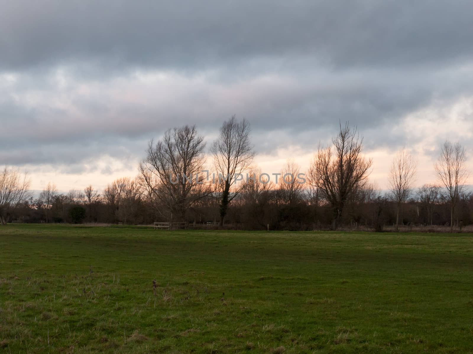 sunset moody sky winter autumn over green field with trees water; essex; england; uk