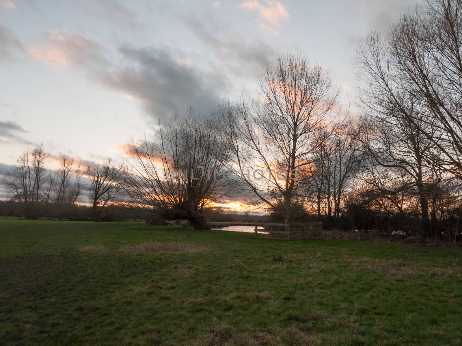 sunset moody sky winter autumn over green field with trees water; essex; england; uk