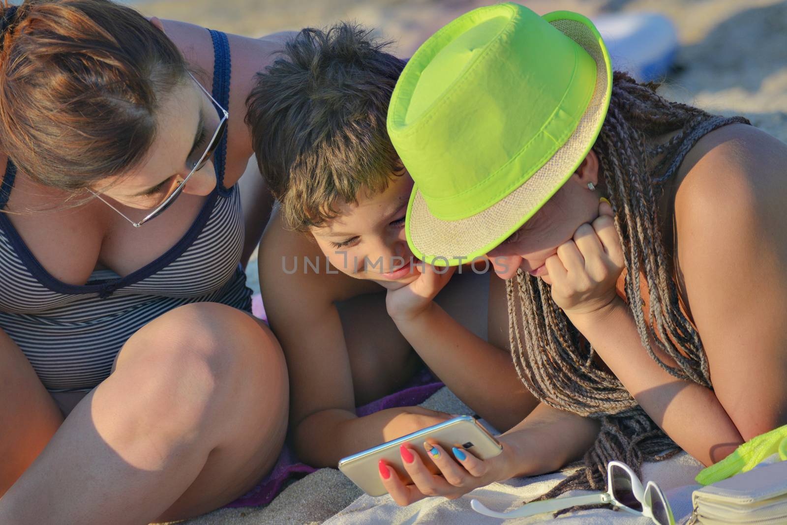 Happy three on the beach - two females and a boy are looking in a smartphone.