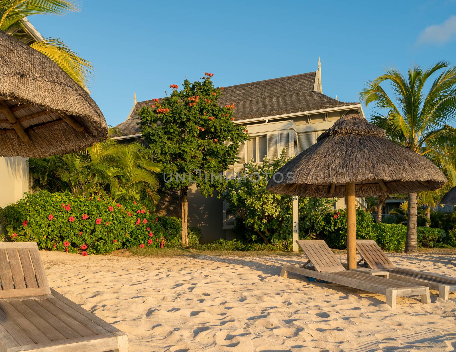 Beach at Mauritius island with wooden parasol,garden and bungalow, sunny day.