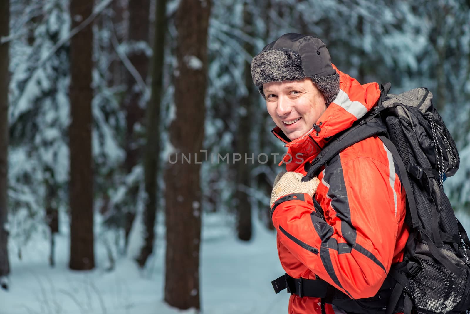 happy tourist in a jacket on a hike with a backpack in the winter forest