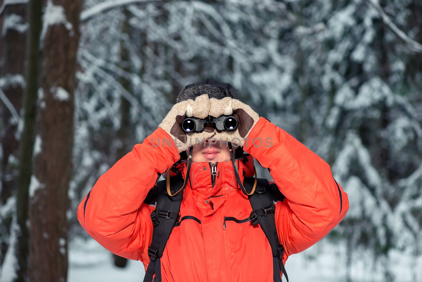 the tourist looks through binoculars, examines the road in the winter forest