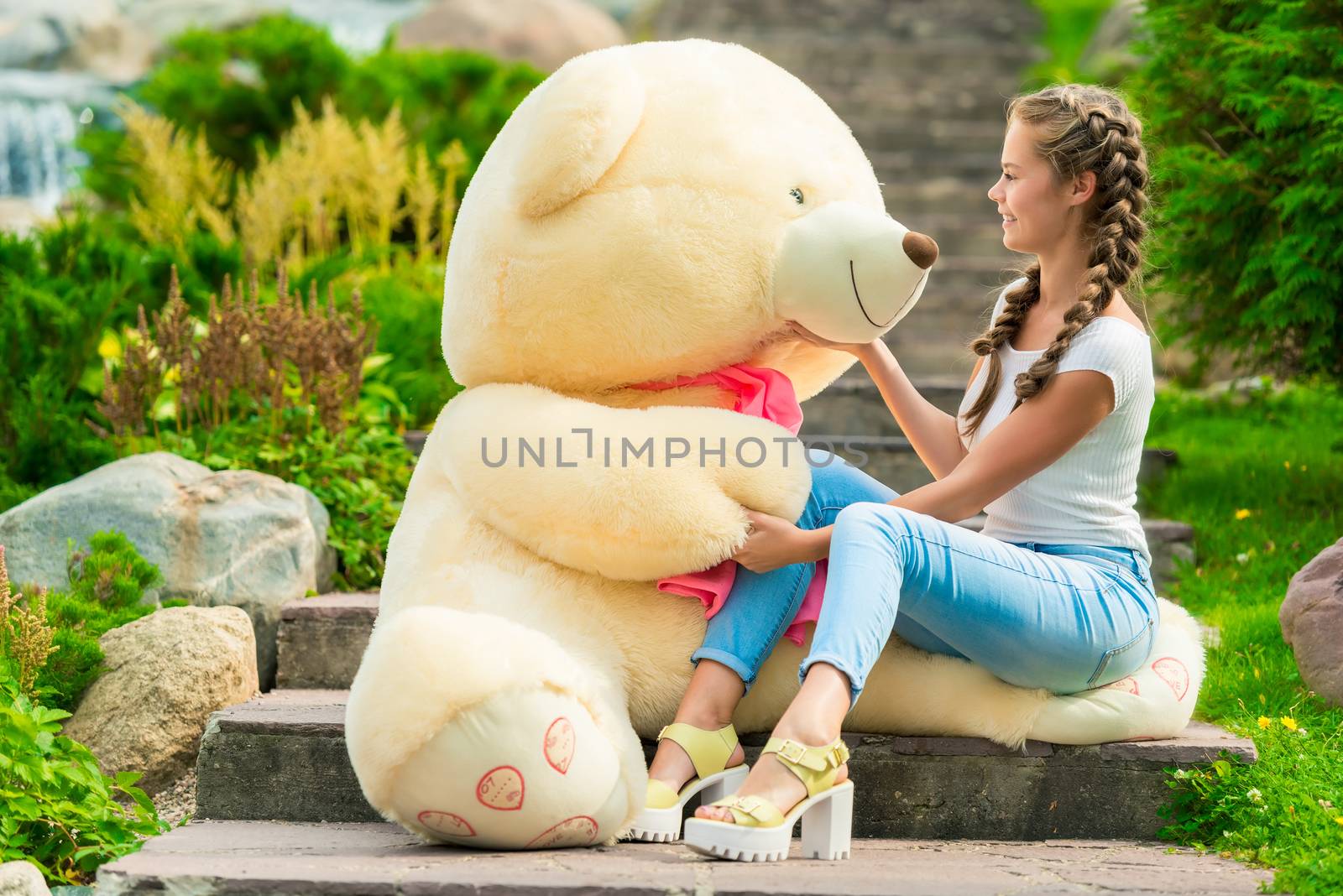 girl with a huge gift - a teddy bear in the park on the stairs