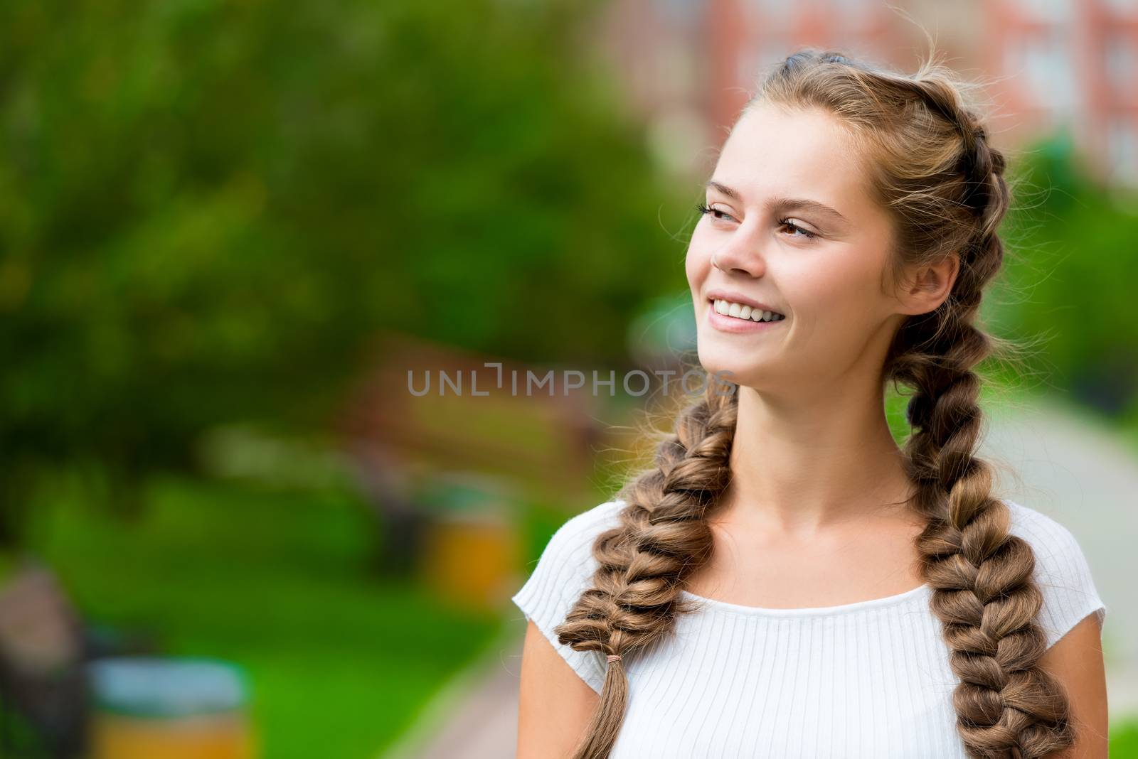 portrait of a beautiful young girl in a white T-shirt with two braids in the park