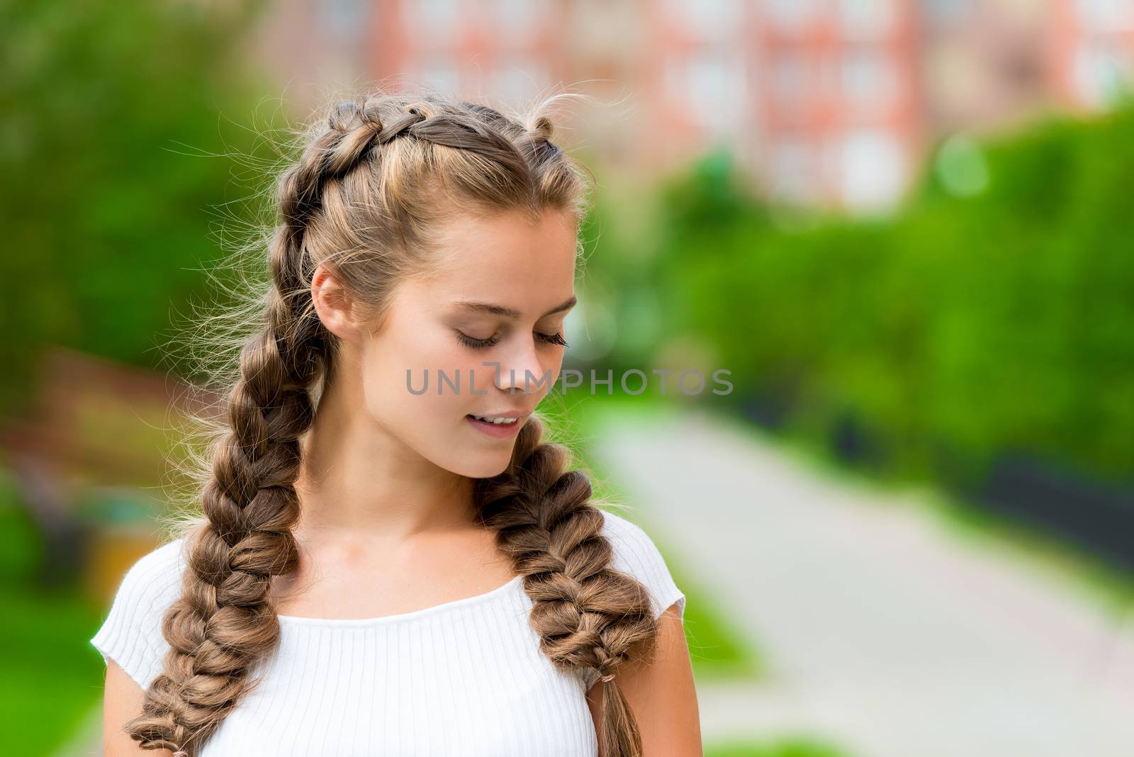 close-up portrait of a young 20 year old woman in a white T-shirt with two braids in the park