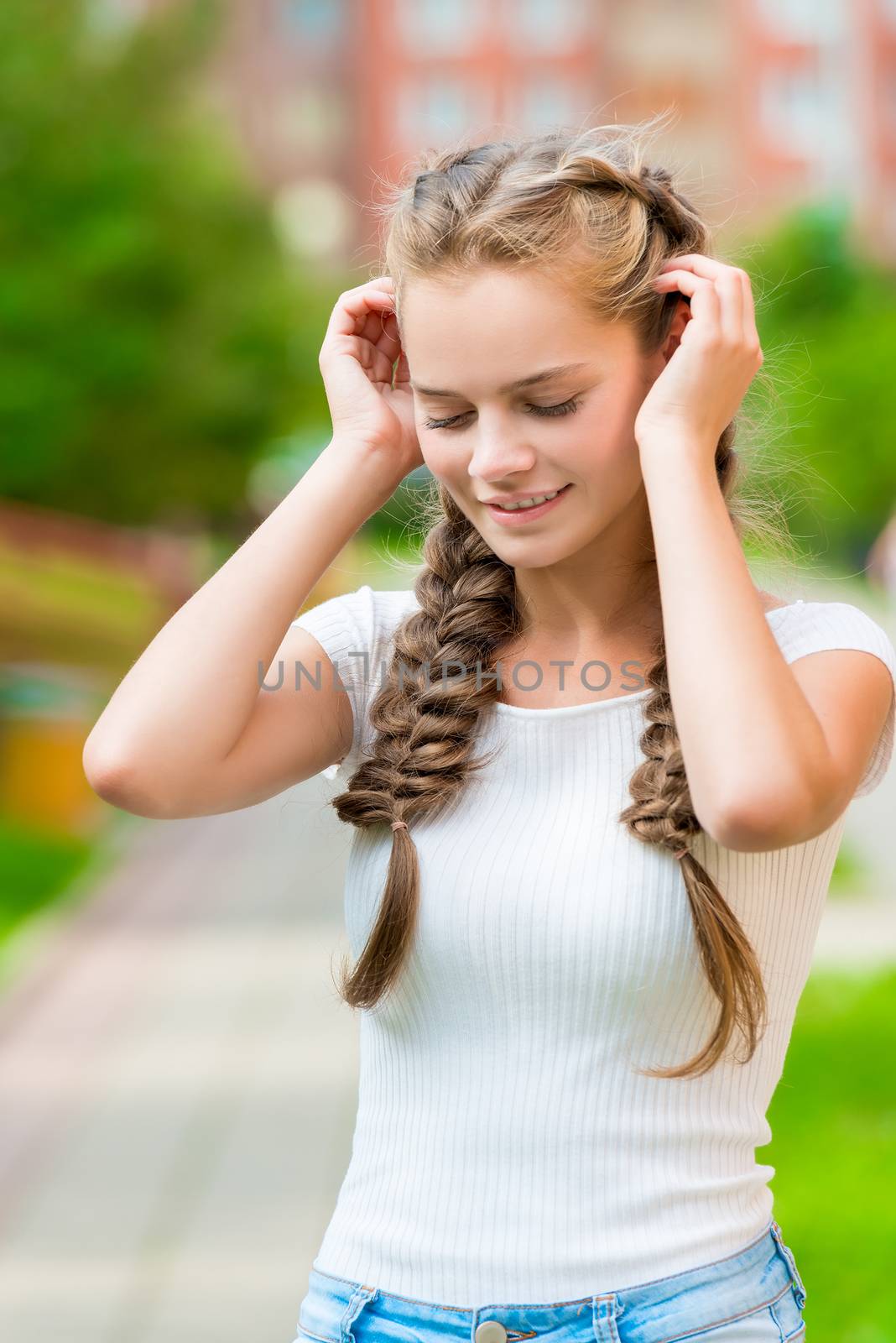 beautiful girl with two braids corrects hands hair, close-up portrait in the park