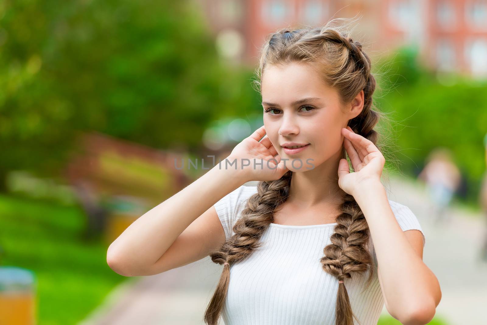 charming young woman with two braids straightens her hair, close-up portrait in the park