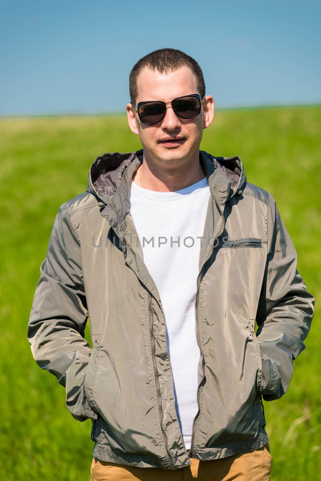 portrait of a man in a jacket and sunglasses on a green meadow by kosmsos111