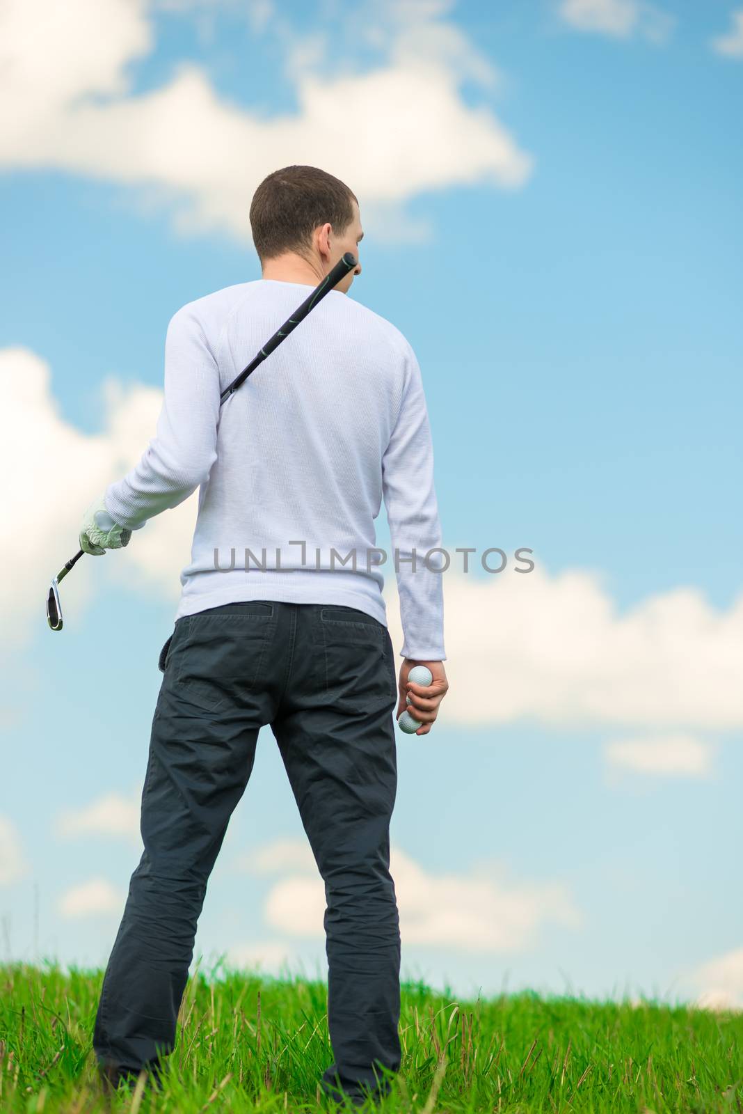 man with a golf club and balls examines the field for the game, the view from the back