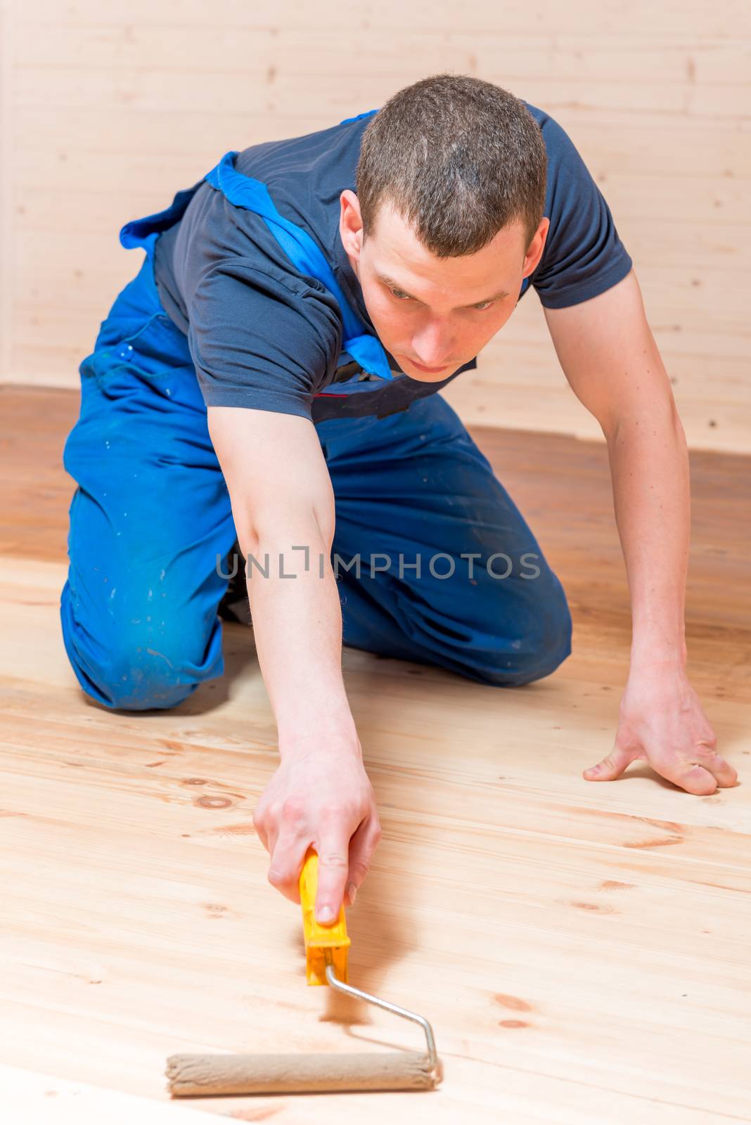 skilled young worker paint roller on a wooden floor in the house