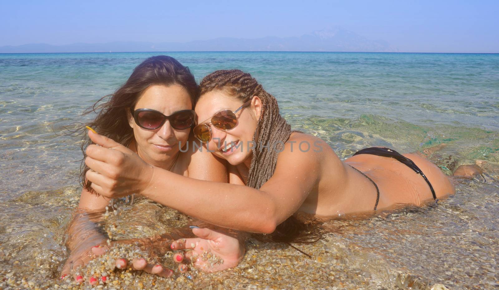 Two beautiful girls on a distant sea shore lying in the water playing with sand.