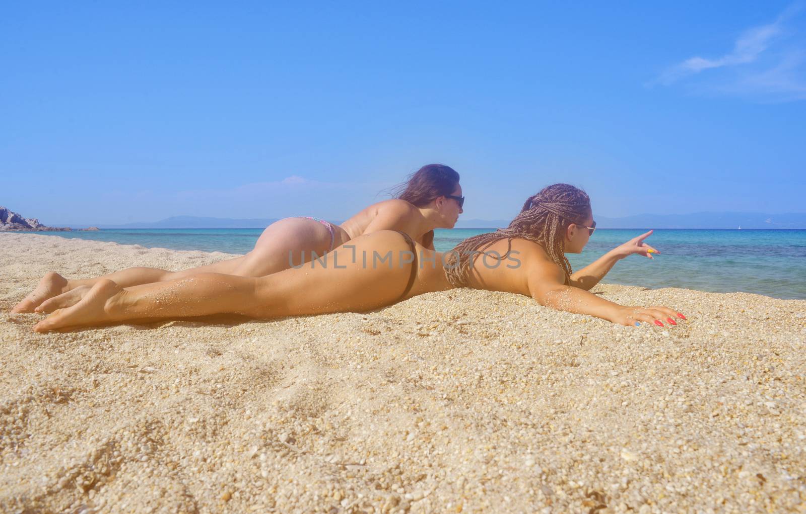 Two beautiful mermaids on a distant sea shore lying on the sand.
