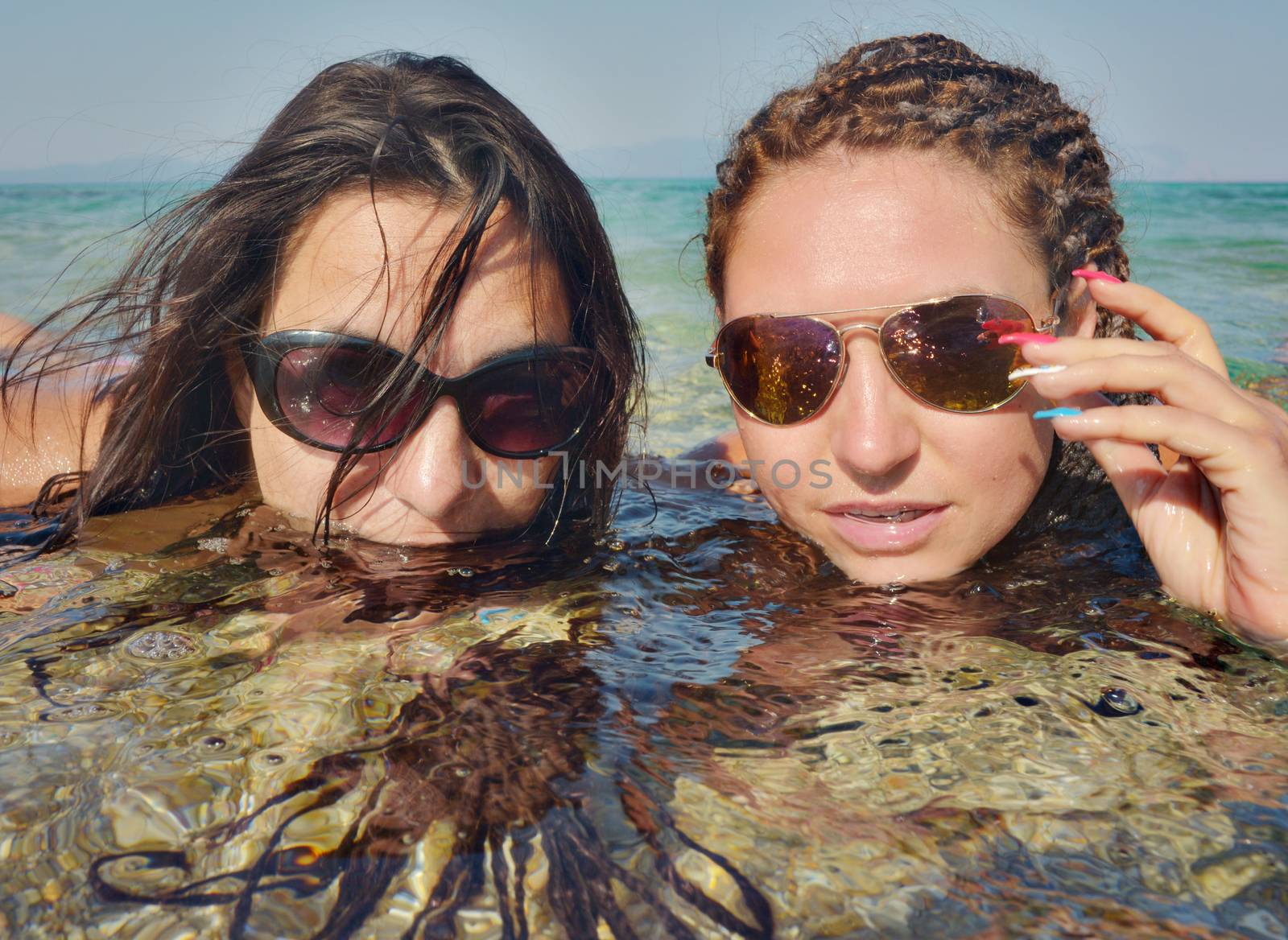 Two beautiful girls on a distant sea shore lying in the water.