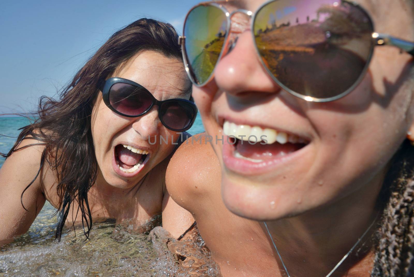 Two female faces - one smiling out of focus and one screaming in sea water.