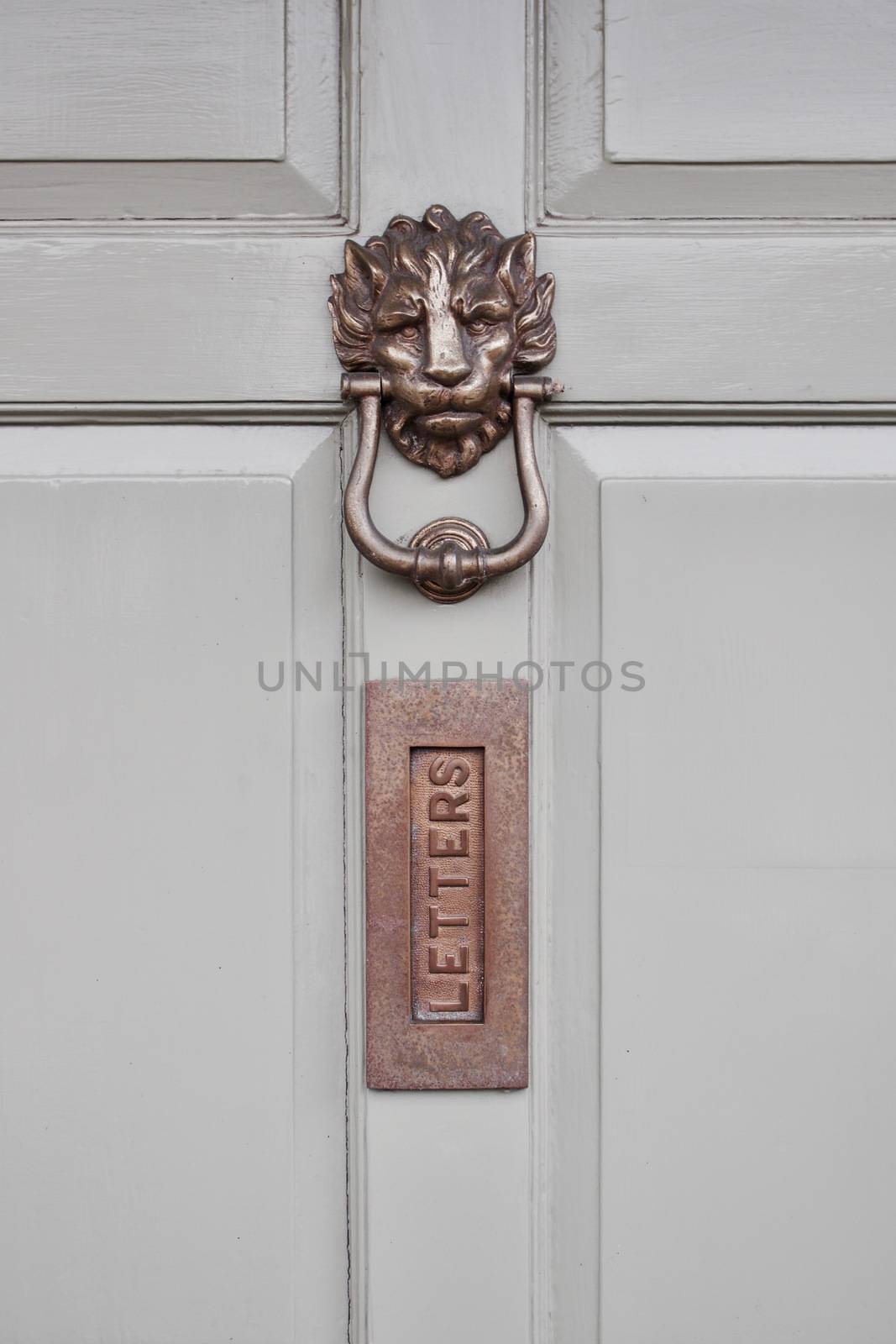 Metal gold lion knocker on white doors near letters metal whole.