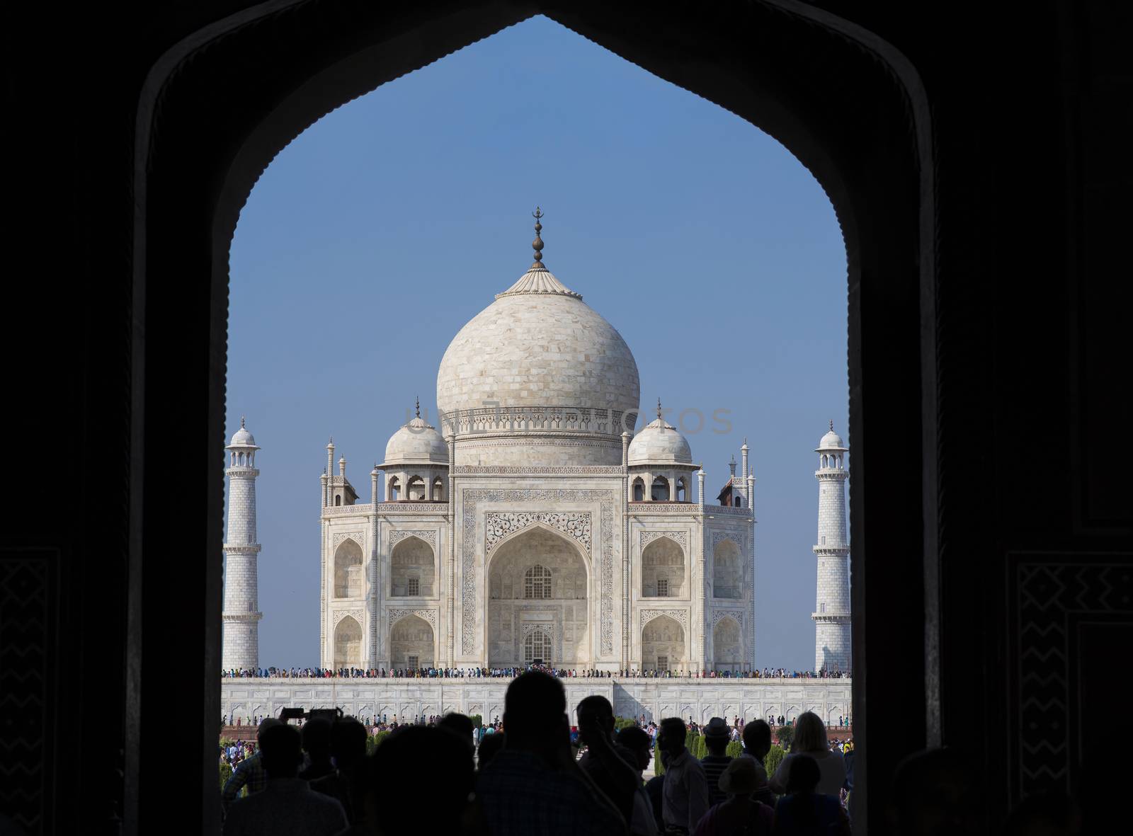 Taj Mahal viewed through entrance gate and silhouette of people going through entry gate to the Taj Mahal complex in Agra, India.