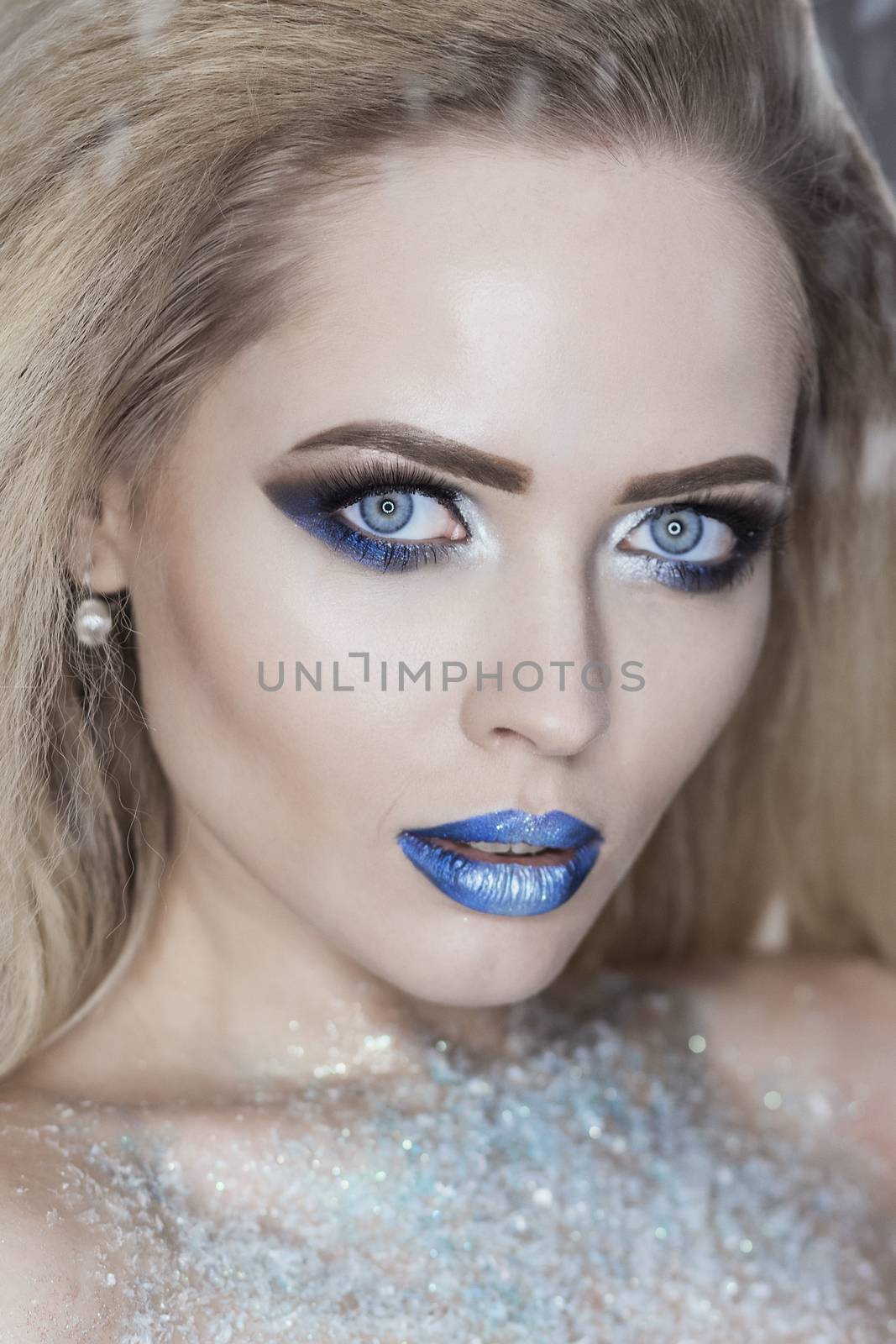 Winter Beauty Woman. Christmas Girl Makeup. Holiday Make-up. Snow Queen High Fashion Portrait over Blue Snow Background.