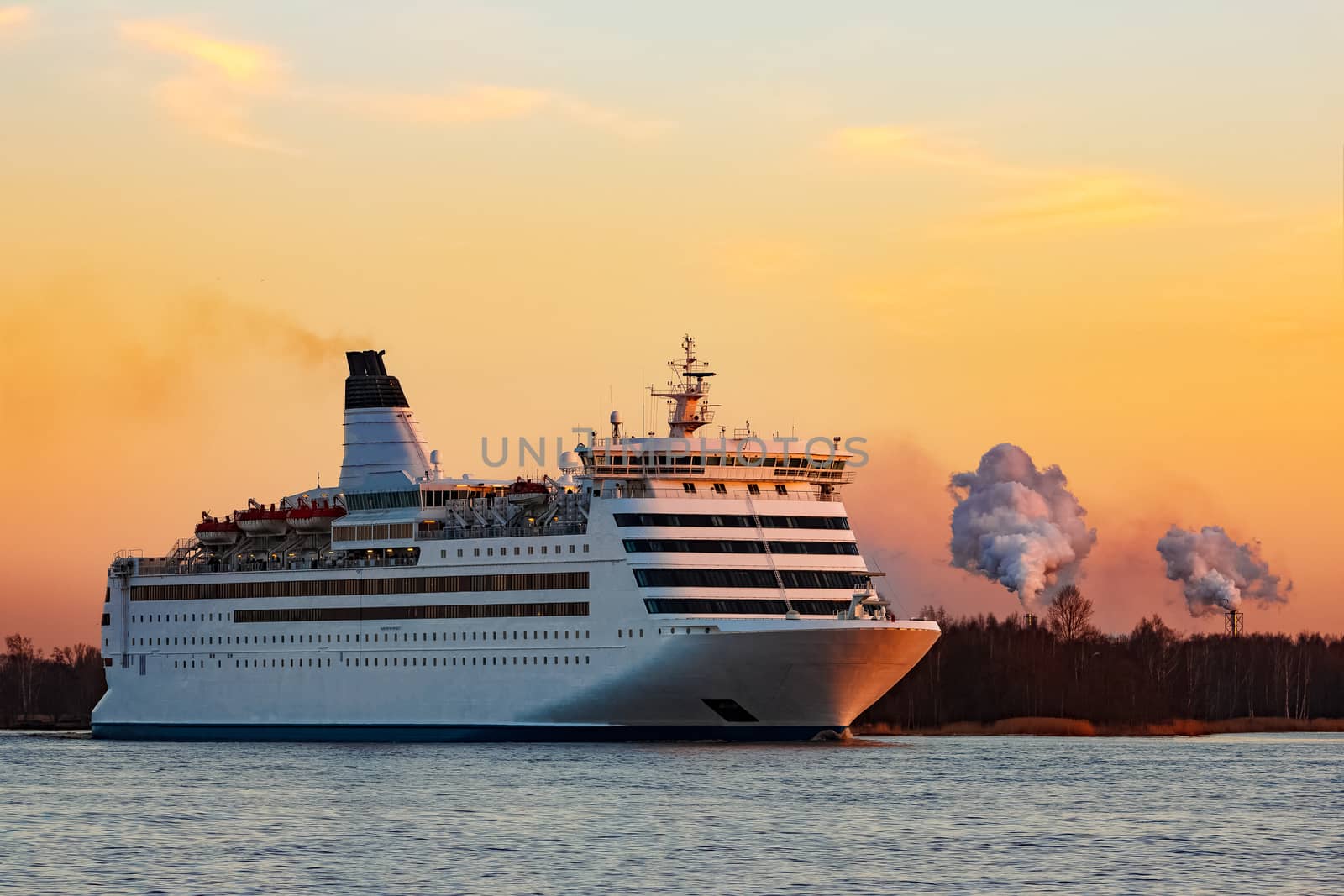 White passenger ship moving against the orange sunset sky