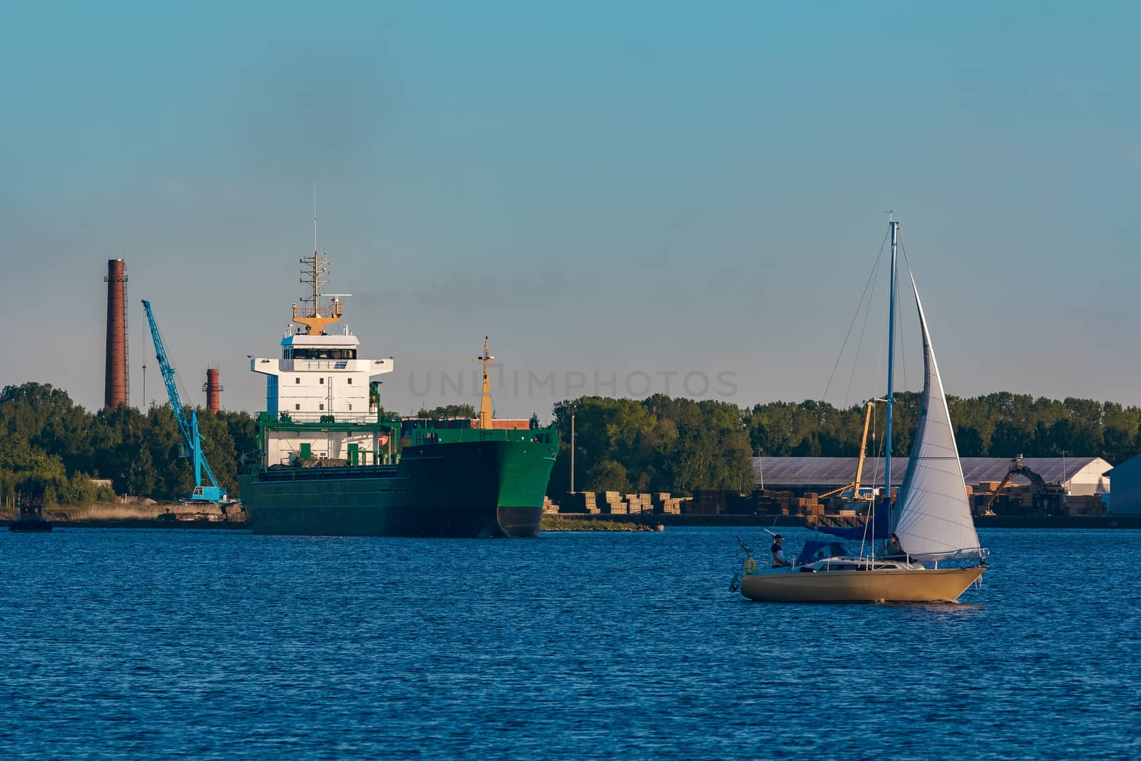 Green cargo ship leaves the port in a clear day